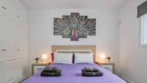 A bedroom with a large bed, two nightstands, a wall-mounted peacock painting, and a window.