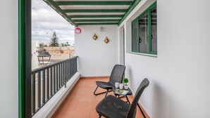 A balcony with two wicker chairs, a small table with a plant, and a window with green trim.