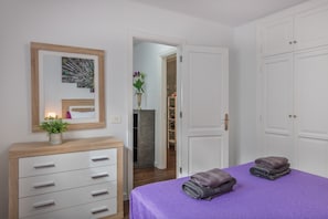 Quarto com colcha roxa, cómoda de madeira, espelho decorado com pena de pavão e porta para um banheiro.