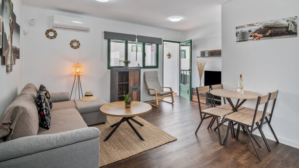 A modern living room with a sofa, a round table, and a dining table with chairs. There is a lamp, a plant, and a fireplace.