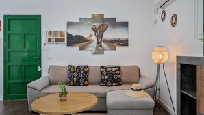 A living room with a green door, a sofa with patterned cushions, a round wooden table, and a floor lamp.