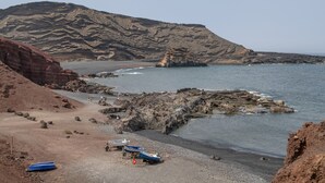 A rocky beach with boats, a clear sky, and a mountainous backdrop.