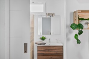 Ein modernes Badezimmer mit einem weißen Waschtisch, einem Spiegel, einem Holzkabinet und einem Blumentopf.