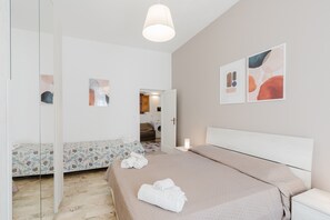 A bedroom with a bed, a bedside table, a mirror, and a door leading to a bathroom.