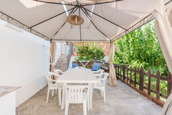 A covered patio with a table and chairs, a hanging light fixture, and a wooden fence.