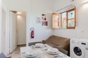 A small, clean room with a table set for dining, a washing machine, and a fire extinguisher on the wall.