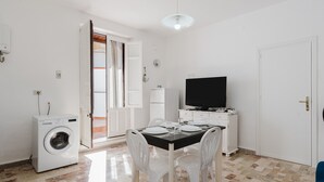 A compact living space with a washing machine, a dining table with chairs, a television, and a door leading to another room. - Apartment 'Sea Nest - Near the Beach' with Private Terrace, Wi-Fi and Air Conditioning (Balestrate)