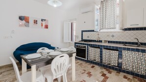 A kitchen with a dining table, chairs, a blue sofa, a tiled backsplash, and a window with curtains. - Apartment 'Sea Nest - Near the Beach' with Private Terrace, Wi-Fi and Air Conditioning (Balestrate)
