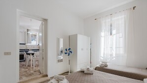 A hotel room with a bed, a bedside table, a mirror, a fan, and a view of the kitchen. - Apartment 'Sea Nest - Near the Beach' with Private Terrace, Wi-Fi and Air Conditioning (Balestrate)