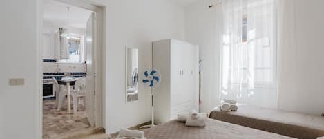 A hotel room with a bed, a bedside table, a mirror, a fan, and a view of the kitchen.