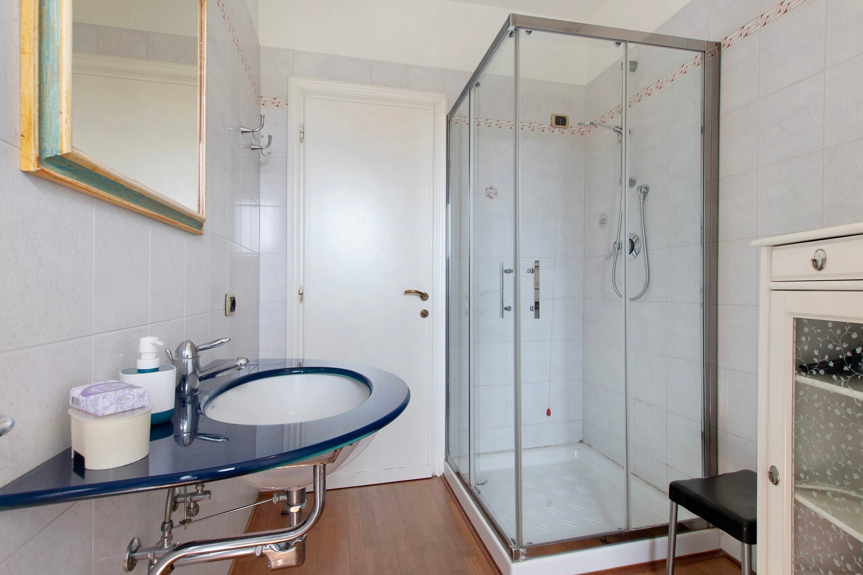 Une salle de bain avec une douche à parois de verre, un lavabo dont le bord est bleu et un miroir avec un cadre doré.