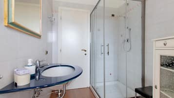 Un baño con ducha envuelta en vidrio, un lavamanos con detalle azul y un espejo con marco dorado.