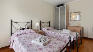 A bedroom with two beds, a wardrobe, a mirror, and a bedside table with a lamp. - Apartment 'Raggio Di Sole' with Balcony and Wi-Fi (Torre del Lago Puccini)