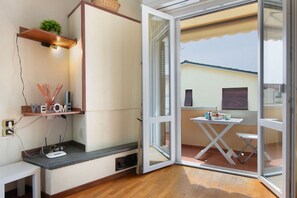 A room with a sliding glass door leading to an outdoor area, a small table with a chair, a shelf with a plant, and a 'WELCOME' sign. - Apartment 'Raggio Di Sole' with Balcony and Wi-Fi (Torre del Lago Puccini)