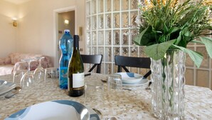 A dining table set with plates, cutlery, and a bottle of wine, with a decorative plant in a glass vase. - Apartment 'Raggio Di Sole' with Balcony and Wi-Fi (Torre del Lago Puccini)