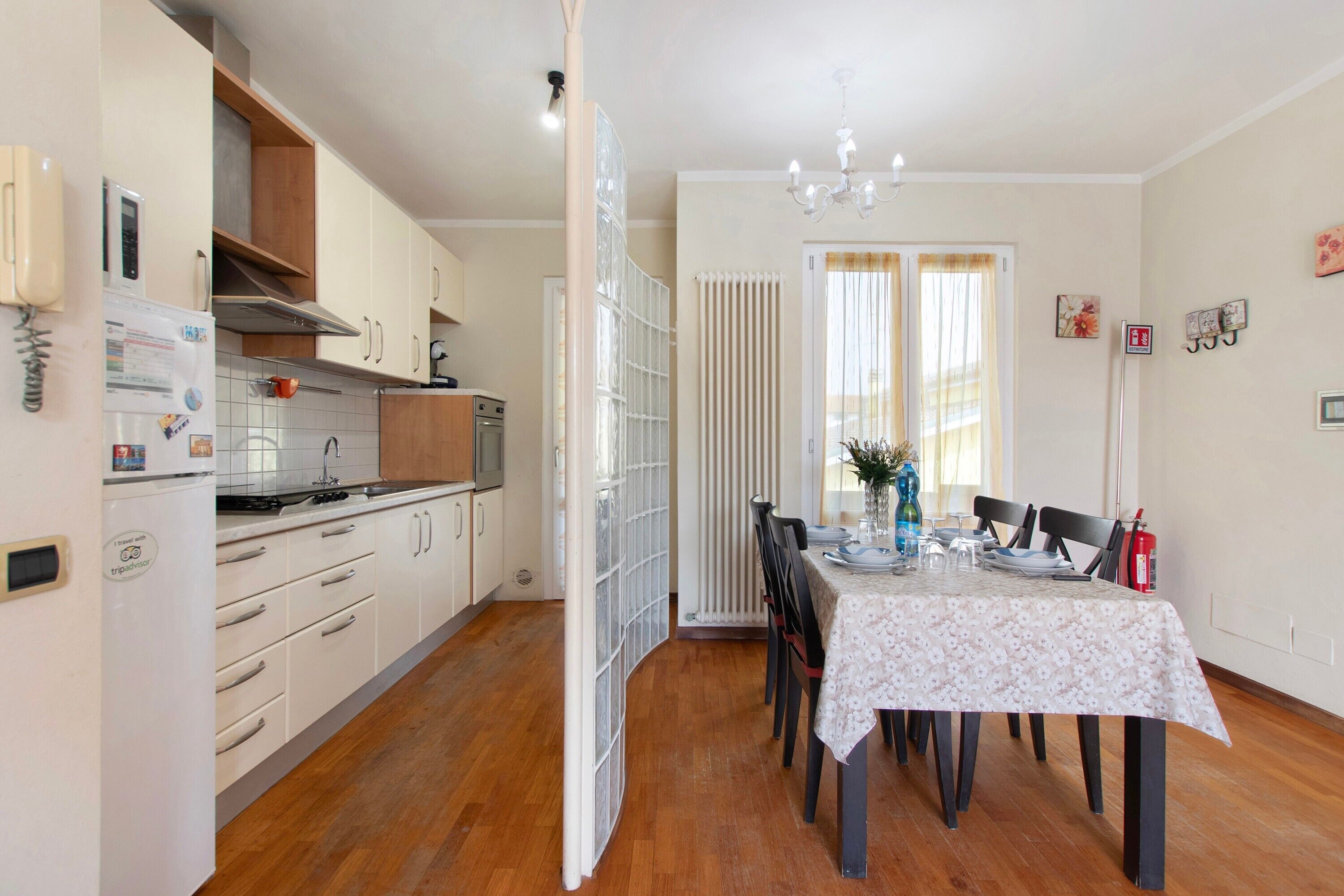 A kitchen with white cabinets, a refrigerator, and a stove. There is a dining table with chairs and a vase of flowers.