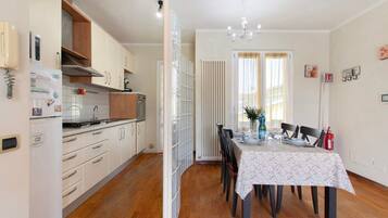 A kitchen with white cabinets, a refrigerator, and a stove. There is a dining table with chairs and a vase of flowers.