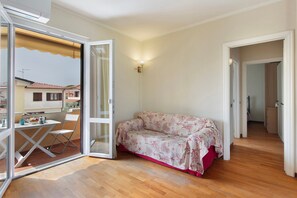 A room with a wooden floor, a sofa with a floral cover, a table with a teapot and cups, and a sliding glass door leading to an outdoor area. - Apartment 'Raggio Di Sole' with Balcony and Wi-Fi (Torre del Lago Puccini)