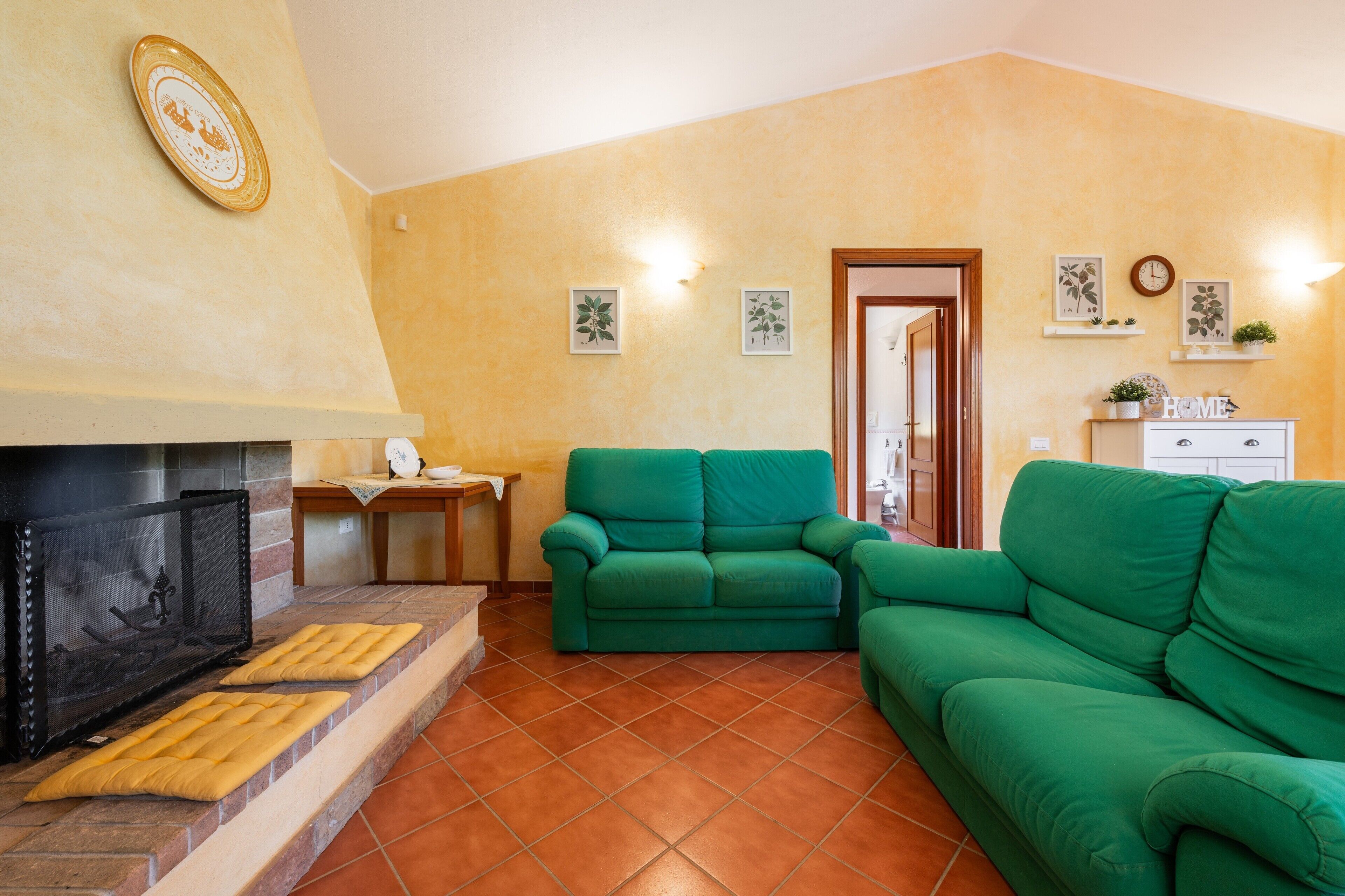 Ein Wohnzimmer mit Kamin, grünen Sofas, einem Holztisch und einer Tür zu einem anderen Raum.