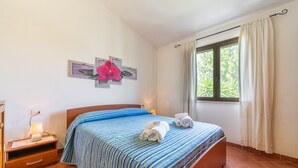 Een slaapkamer met een bed, nachtkastje, raam met gordijnen en een kunstwerk aan de muur.