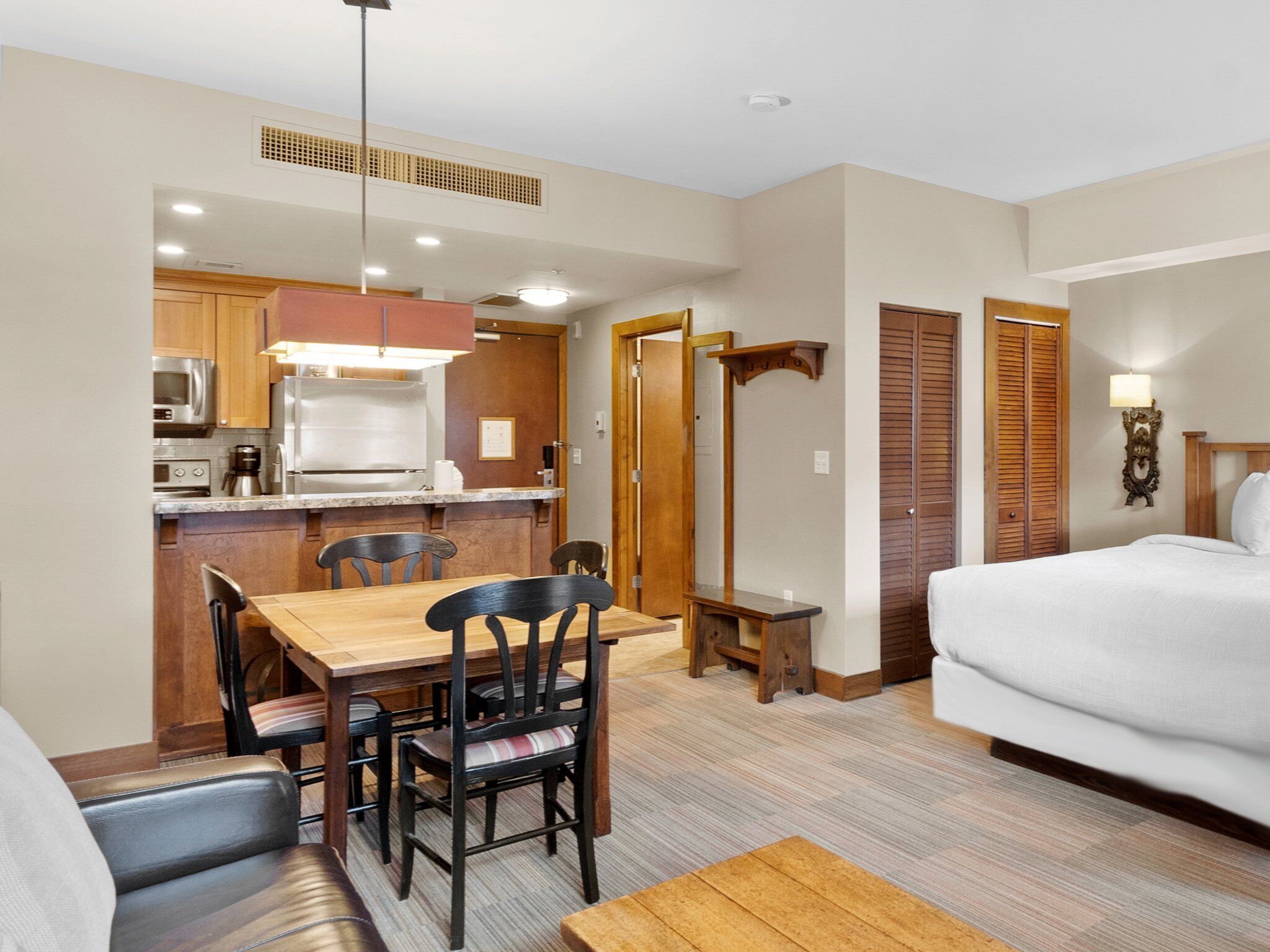 A compact hotel room with a dining area, kitchenette, and a bed.