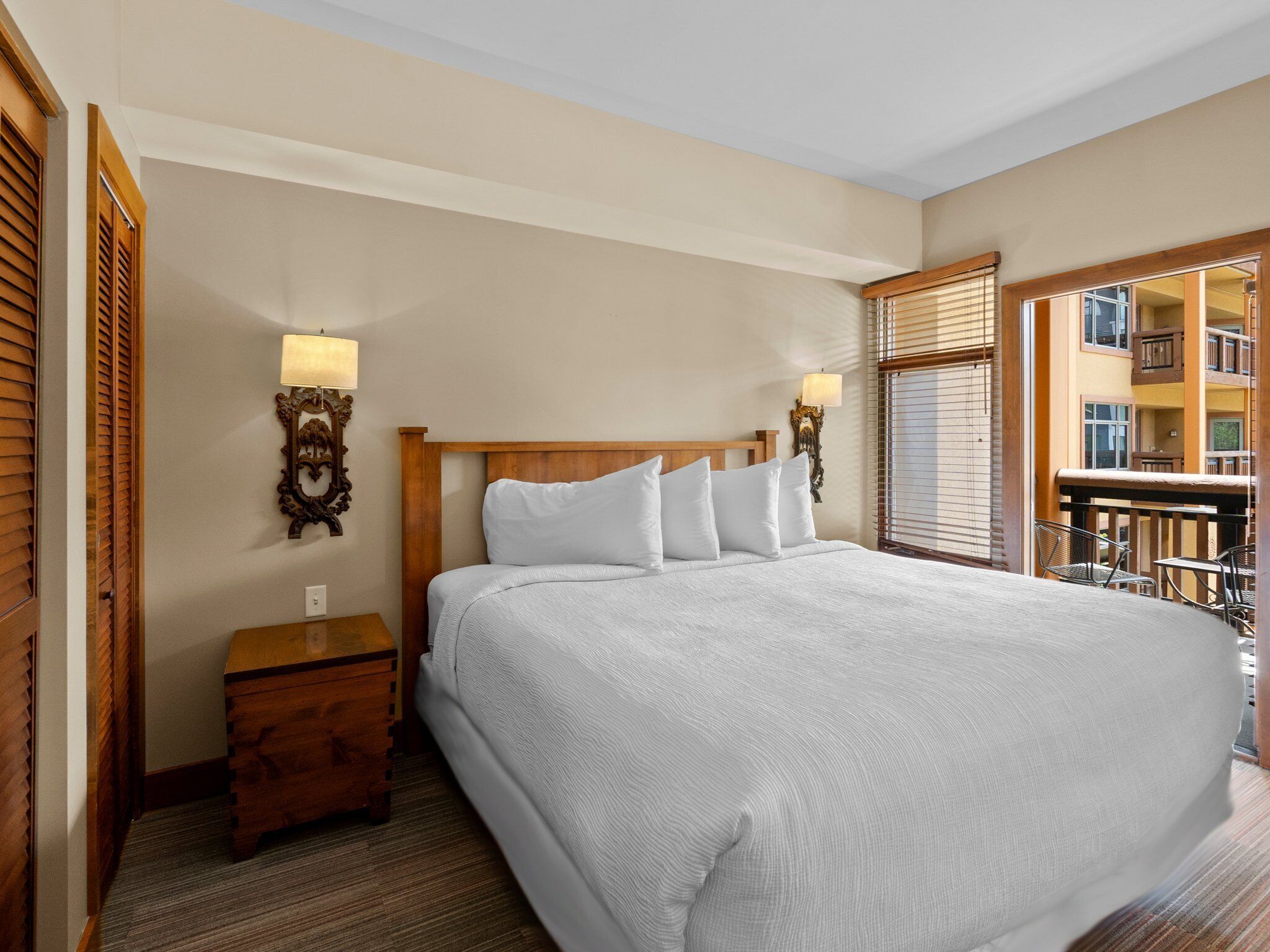 Une chambre d’hôtel avec un grand lit, une tête de lit en bois, deux tables de chevet et un balcon offrant une vue sur l’immeble.
