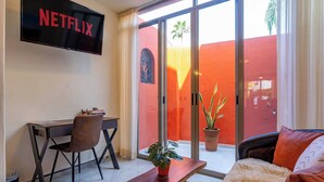 Una sala de estar moderna con una televisión de pantalla plana montada en la pared, un escritorio de madera con una silla, un sofá y una planta en maceta.