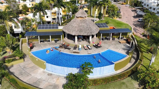 Una piscina circular con un centro techado de paja, rodeada de sillas de descanso y una zona de estar cubierta.