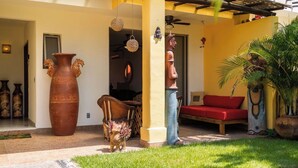 Un espacio exterior cubierto con un sofá rojo, una maceta de terracota grande y una escultura de madera.