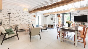 A spacious living area with a stone wall, a dining table, and modern furniture. - Holiday Home 'L'authentik' with Mountain View, Private Terrace and Air Conditioning (Accous)