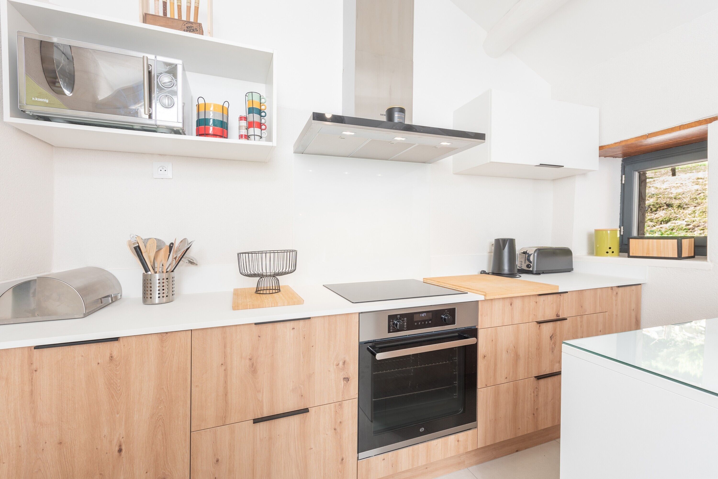 A modern kitchen with a microwave, toaster, oven, wooden cabinets, and a window.