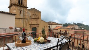 Un balcón con una mesa dispuesta para dos personas, una botella de vino y una bandeja de frutas.