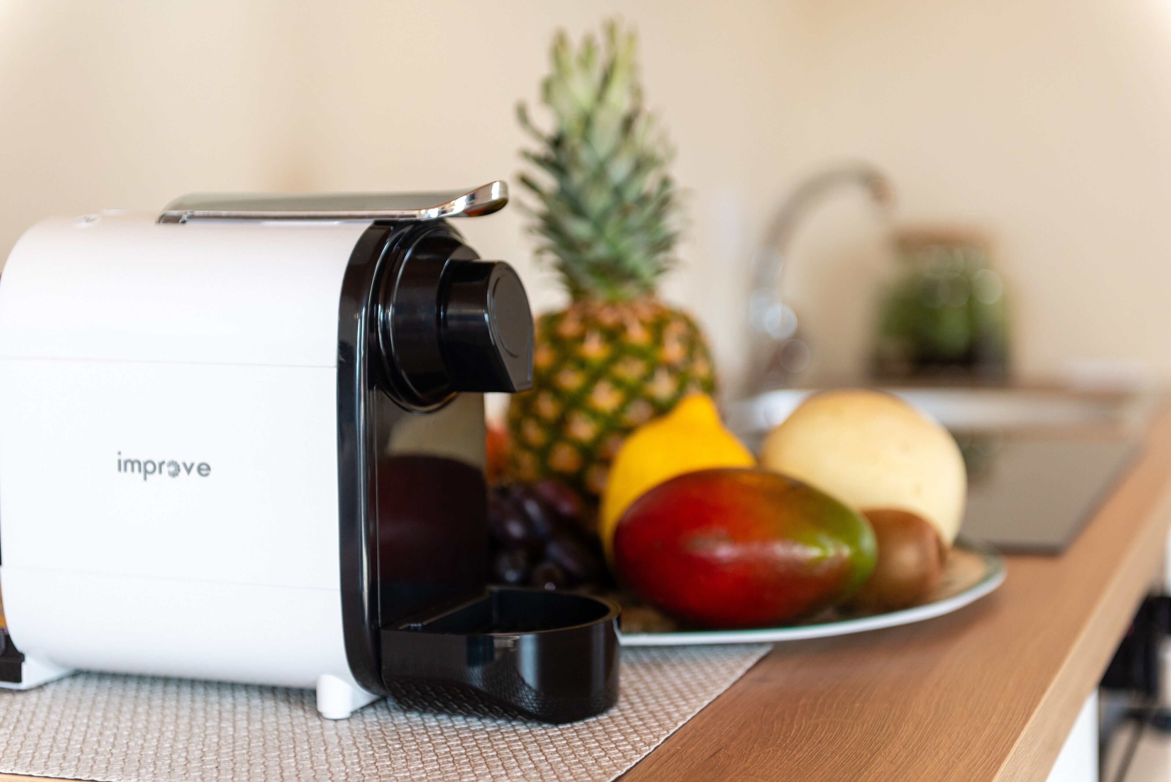 A kitchen with a fruit juicer, a pineapple, and a plate of fruit.