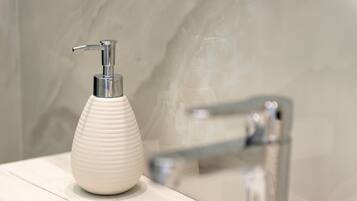 A bathroom with a white textured soap dispenser on a wooden surface, a chrome faucet, and a marble wall.
