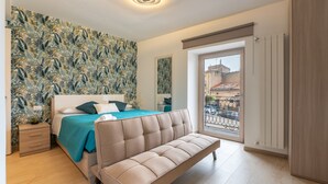 A bedroom with a bed, a sofa, a window with a view, and a patterned wall.