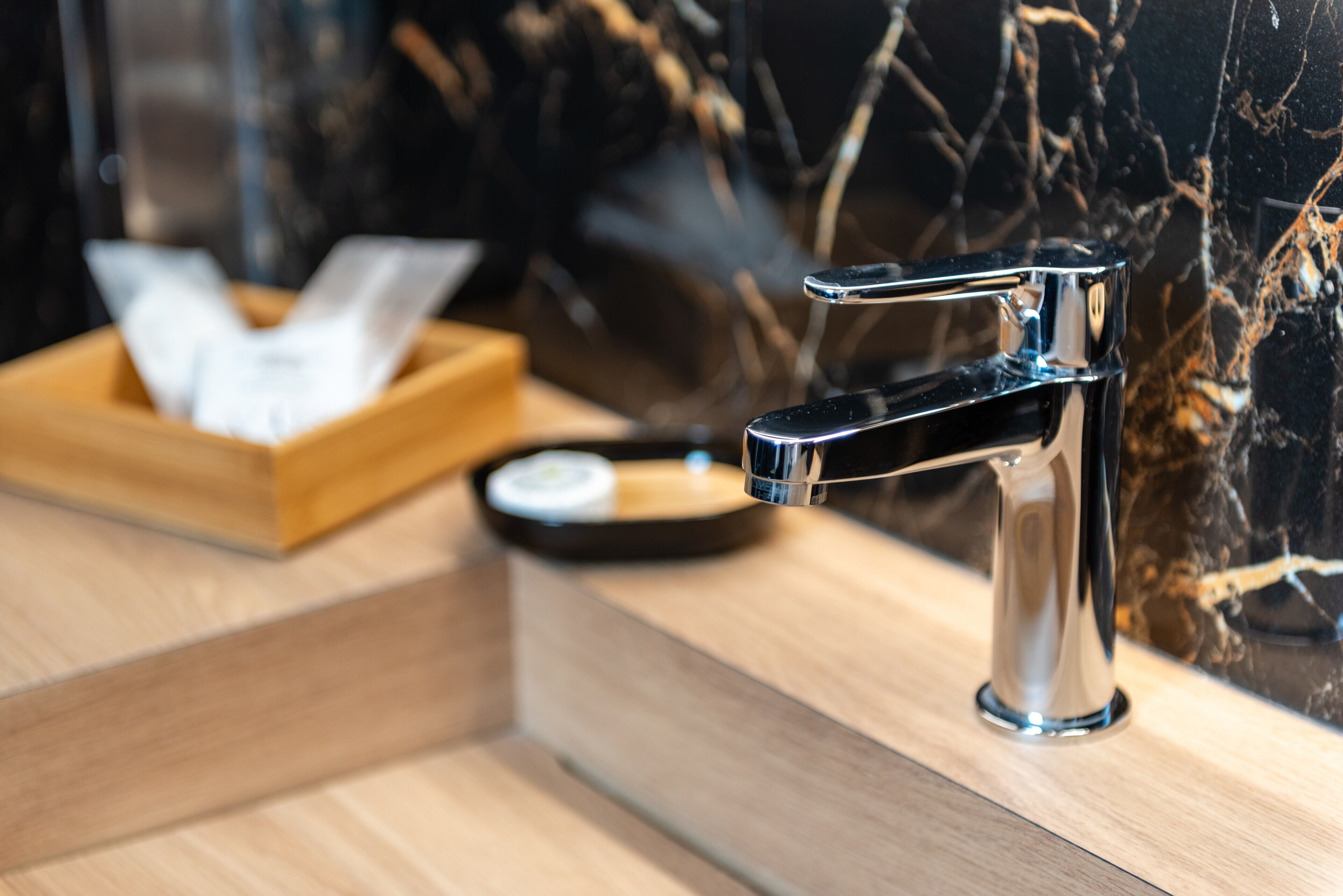 Un baño moderno con grifo cromado, bandeja de madera y pared de mármol.