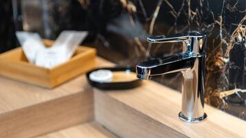 Un baño moderno con grifo cromado, bandeja de madera y pared de mármol.