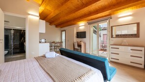 A bedroom with a bed, a desk, a television, and a sliding door leading to a balcony.