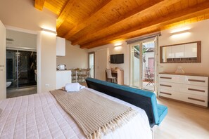 A bedroom with a bed, a desk, a television, and a sliding door leading to a balcony.