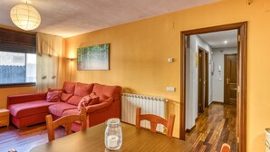 Una sala de estar con un sofá rojo, sillas de madera, una mesa de comedor, un tarro de vidrio, una lámpara y un cuadro en la pared.