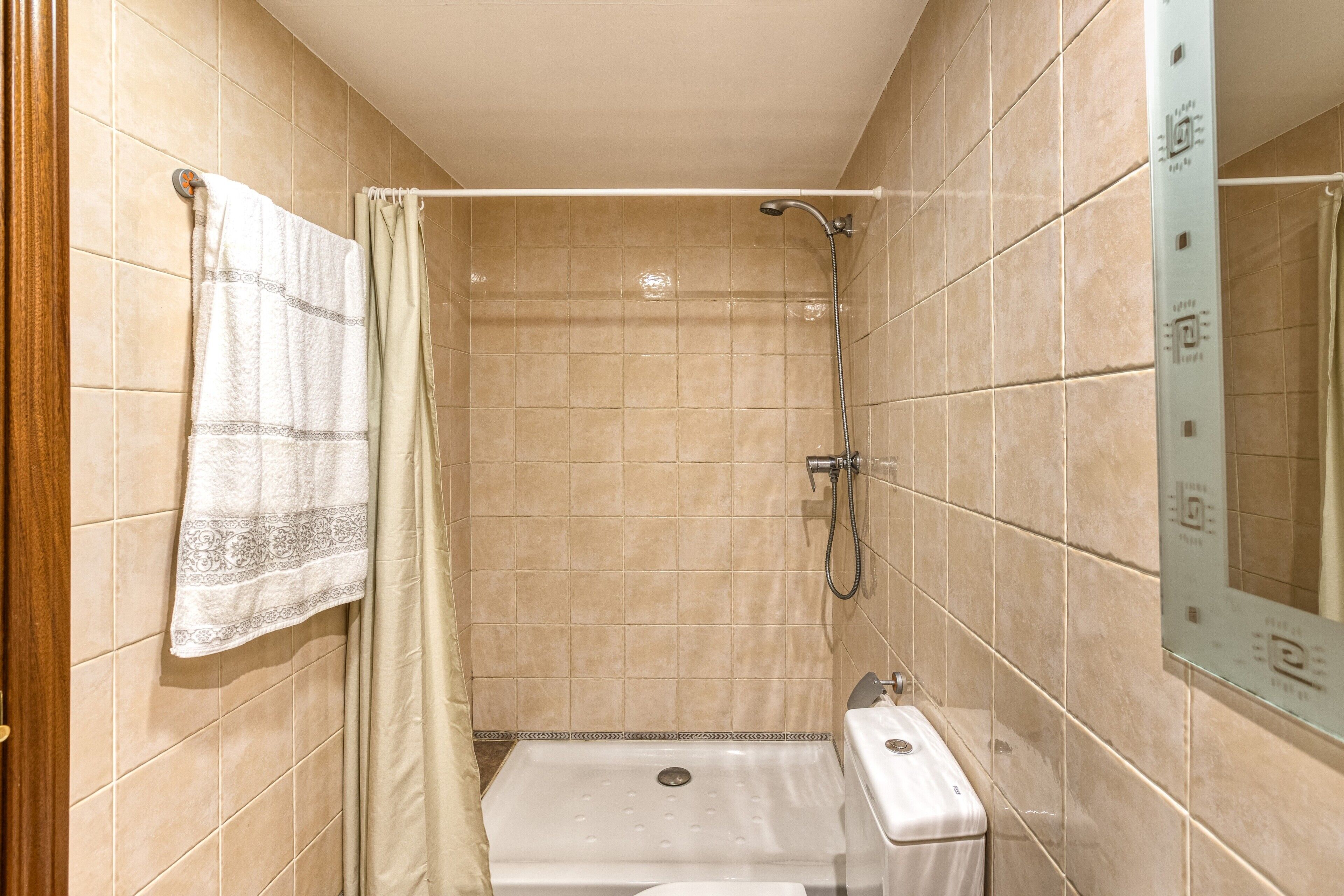 Un baño pequeño con azulejos, un cabezal de ducha, una alcachofa de ducha y un inodoro.