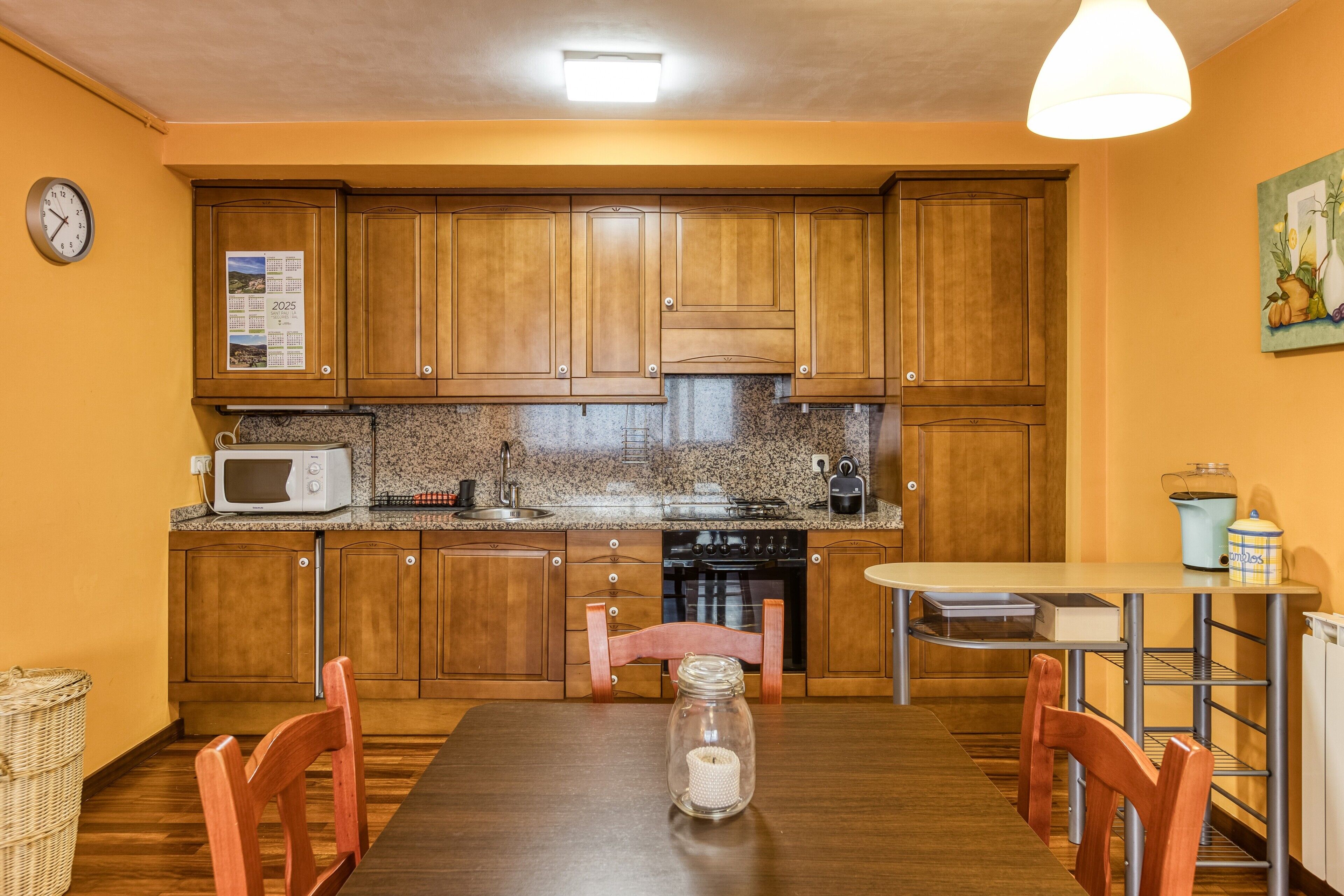 A compact kitchen with wooden cabinets, a microwave, a stove, and a dining table with chairs.