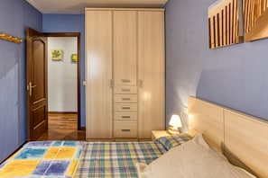 Une chambre à coucher comprenant un lit, une armoire, une table de chevet avec une lampe et une porte donnant sur une autre pièce.