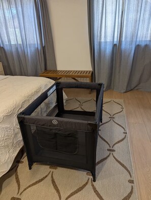 A compact, dark-colored, foldable storage unit with a mesh pocket, placed on a patterned rug in a room with a bed and a small wooden table.
