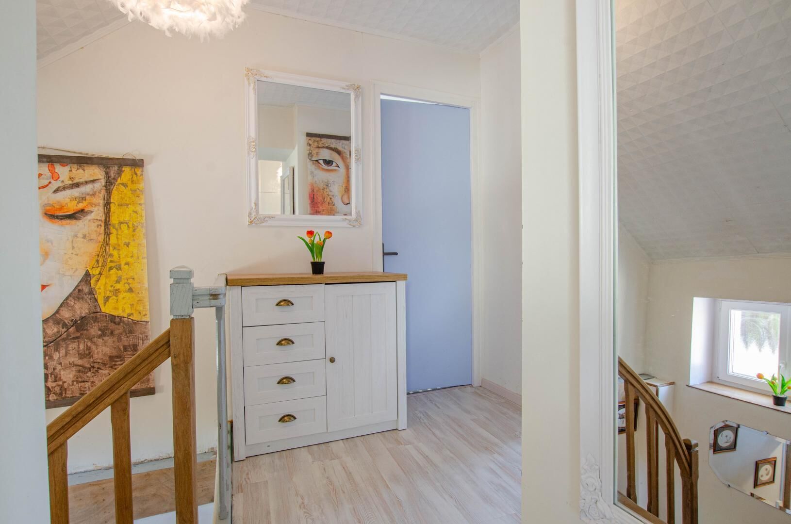 A hallway with a white cabinet, a mirror, and a painting on the wall.