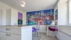 Een moderne keuken met een stadsgezicht muurschildering, barstoelen en een koelkast.