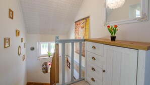 Een hal met een houten trap, een wit plafond en een spiegel aan de muur.