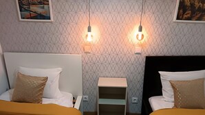 Habitación de hotel con dos camas, una mesita de noche, una pequeña mesa y dos lámparas fijadas a la pared.