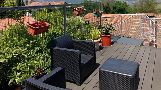 Un patio en la azotea con mobiliario de mimbre, plantas en macetas y vistas a colinas distantes.