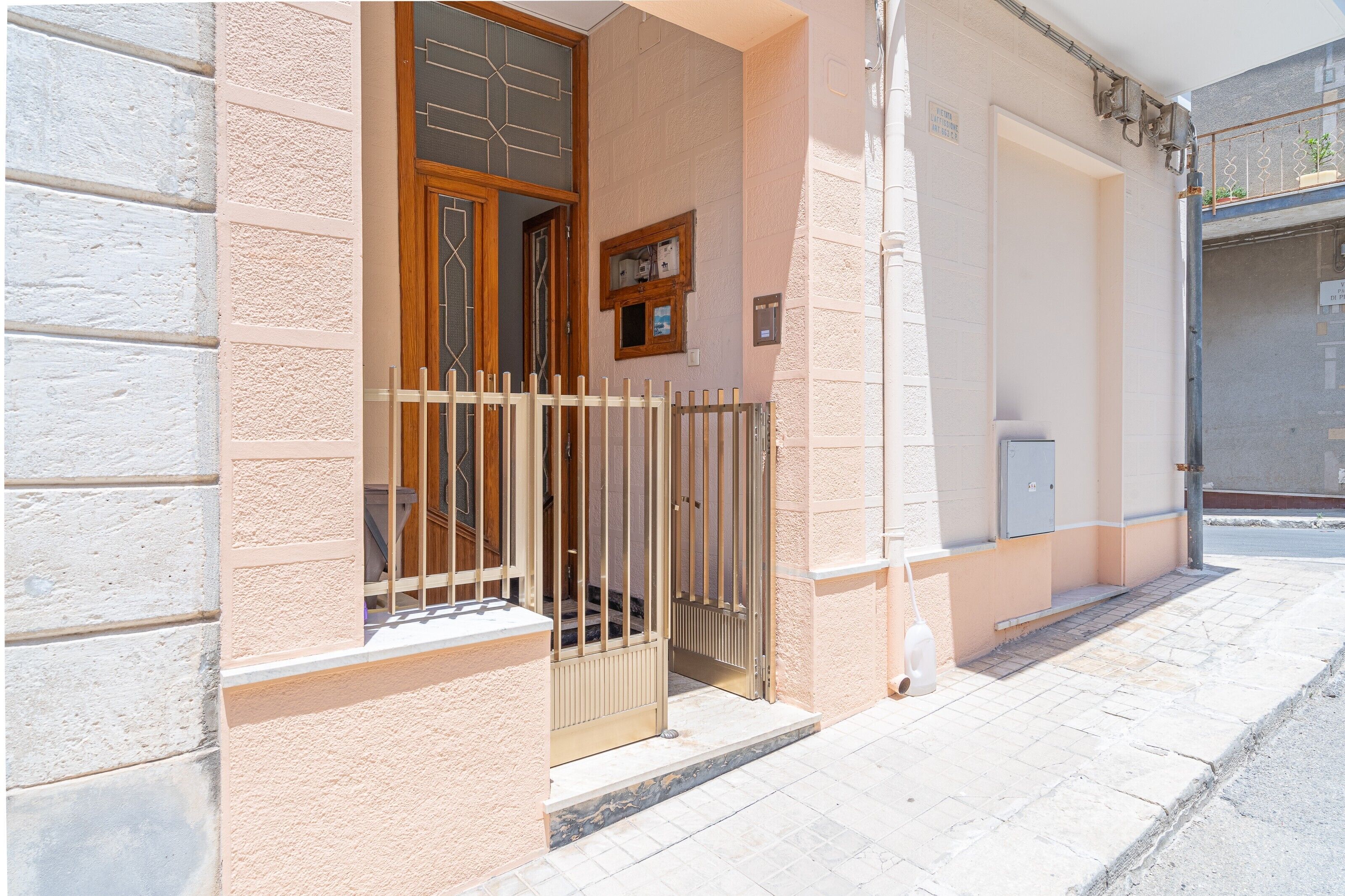 Une entrée d’immeuble avec une porte grillagée, une petite fenêtre et un luminaire fixé au mur.